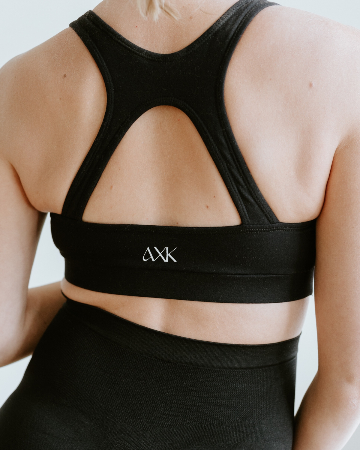 Back view of a black high-impact, racerback, maternity and nursing sports bra paired with matching high-waist leggings. Premium maternity athletic and activewear by AXK.