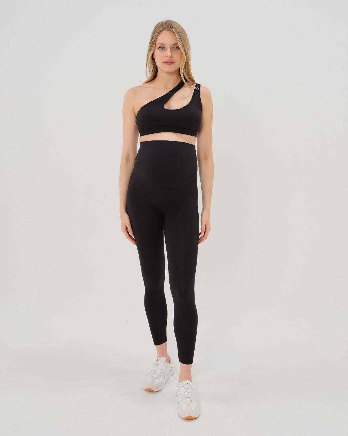 Pregnant woman wearing our best reviewed premium black maternity leggings for 2026 with a matching trendy one shoulder nursing sports bra. Premium maternity athletic and activewear by AXK, available in plus sizes. Petite and tall friendly.