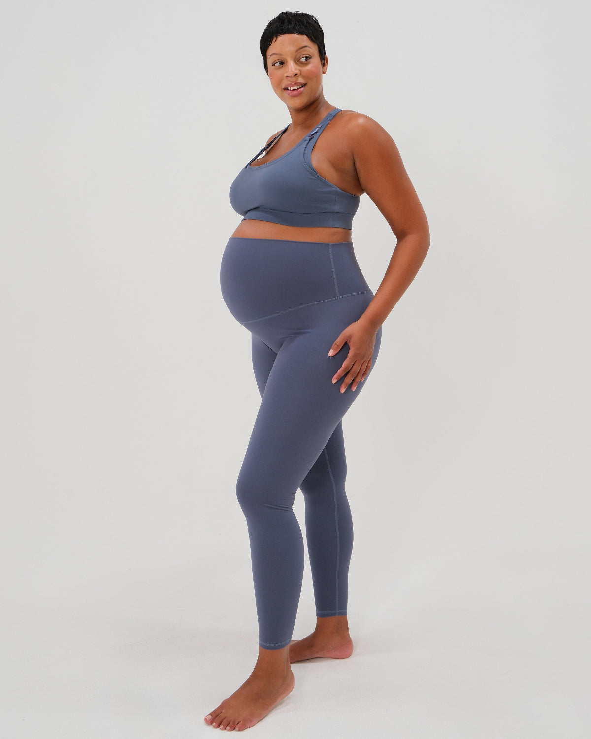Pregnant woman wearing our best reviewed premium brown maternity leggings for 2026 with a flattering scrunch butt and matching trendy one shoulder nursing sports bra, standing against a white background. Premium maternity athletic and activewear by AXK.