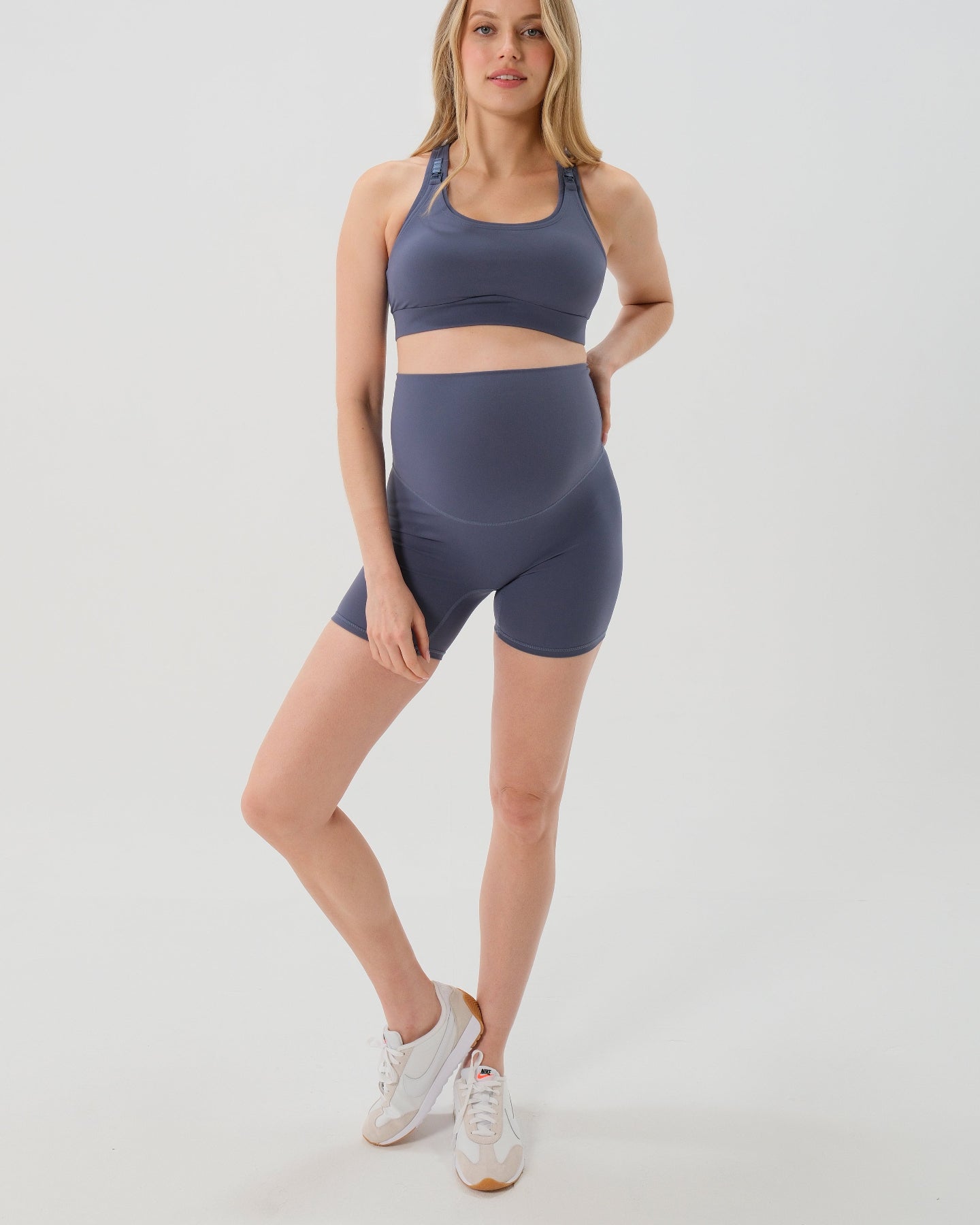 Pregnant woman wearing premium blue maternity bike shorts with a supportive high waist and matching high-impact, racerback maternity and nursing sports bra. Best reviewed 2026 premium maternity athletic and activewear by AXK, petite and tall friendly, in regular and plus size options.