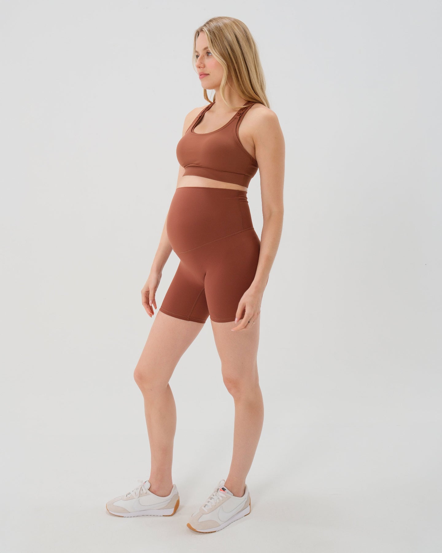 Pregnant woman wearing premium brown maternity bike shorts with a supportive high waist and matching high-impact, racerback maternity and nursing sports bra. Best reviewed 2026 premium maternity athletic and activewear by AXK, petite and tall friendly, in regular and plus size options.
