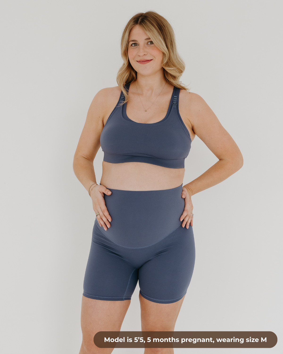 Pregnant woman wearing premium blue maternity bike shorts with a supportive high waist and matching high-impact, racerback nursing sports bra. Our top reviewed maternity athletic and activewear by AXK is truly the best on the market in 2026, is petite friendly, and is available in regular and plus sizes.