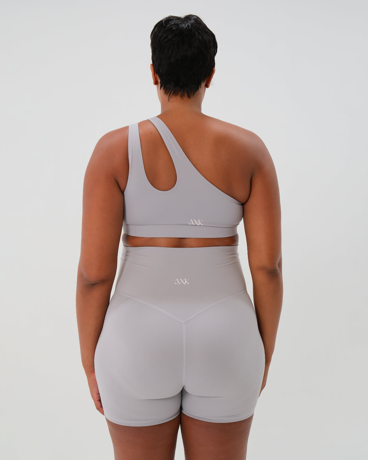 Back view of Light gray one-shoulder maternity and nursing sports bra and matching leggings. The bra features one-handed clip access for easy breastfeeding. Premium maternity activewear by AXK is offered in petite and plus size.