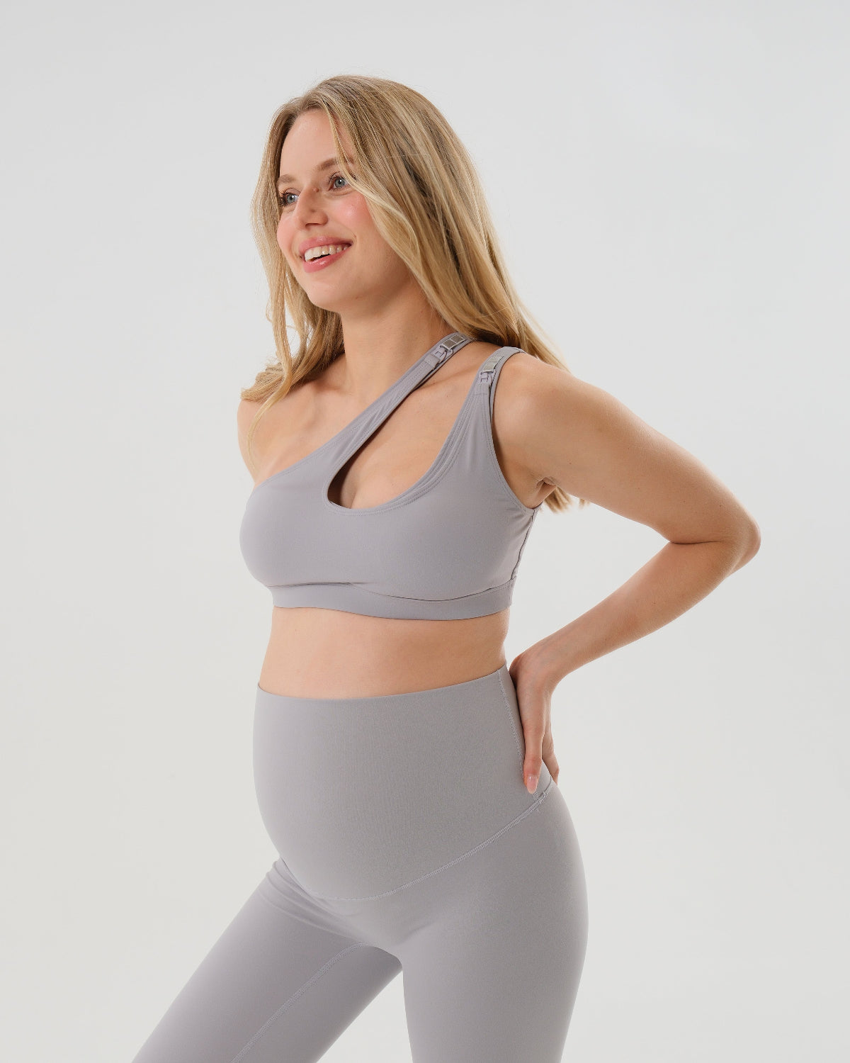 Light gray one-shoulder maternity and nursing sports bra and matching leggings. The bra features one-handed clip access for easy breastfeeding. Premium maternity activewear by AXK is offered in petite and plus size.