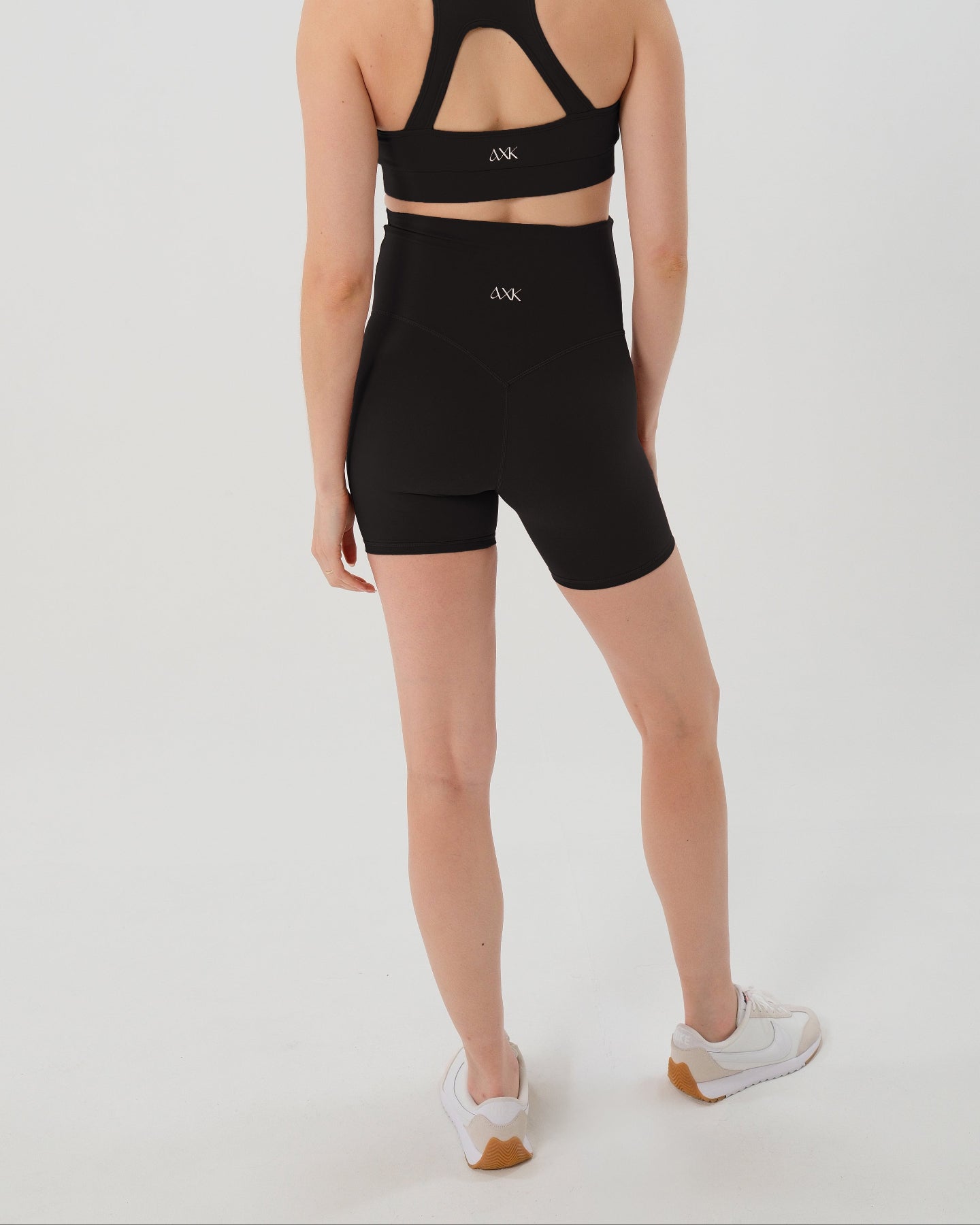 Pregnant woman wearing premium black maternity bike shorts with a supportive high waist and matching high-impact, racerback maternity and nursing sports bra. Best reviewed 2026 premium maternity athletic and activewear by AXK, petite and tall friendly, in regular and plus size options. 
