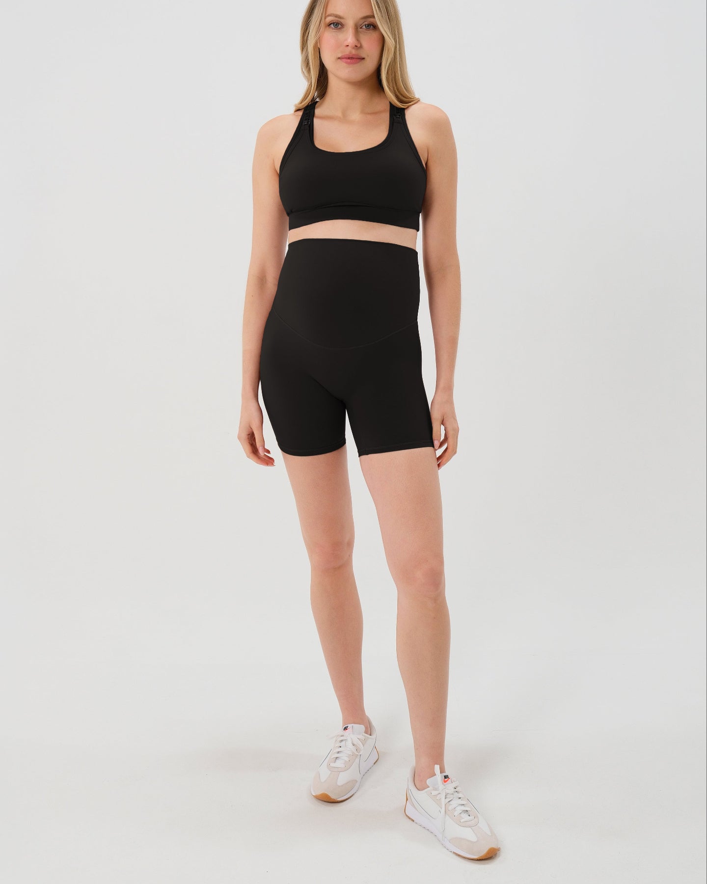 Pregnant woman wearing premium black maternity bike shorts with a supportive high waist and matching high-impact, racerback maternity and nursing sports bra. Best reviewed 2026 premium maternity athletic and activewear by AXK, petite and tall friendly, in regular and plus size options. 