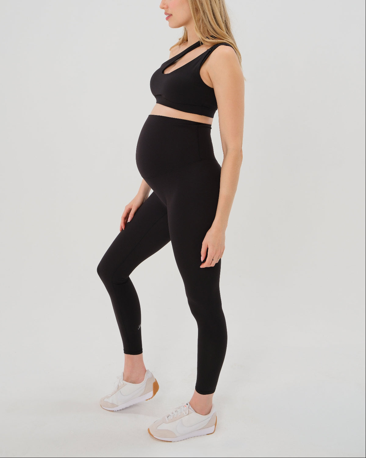 Pregnant woman wearing our best reviewed premium black maternity leggings for 2026 with a flattering scrunch butt and matching trendy one shoulder nursing sports bra. Perfect for running, pregnancy yoga, lounge wear, and walking or hiking. Premium maternity athletic and activewear by AXK available in regular and plus sizes, petite and tall friendly. 