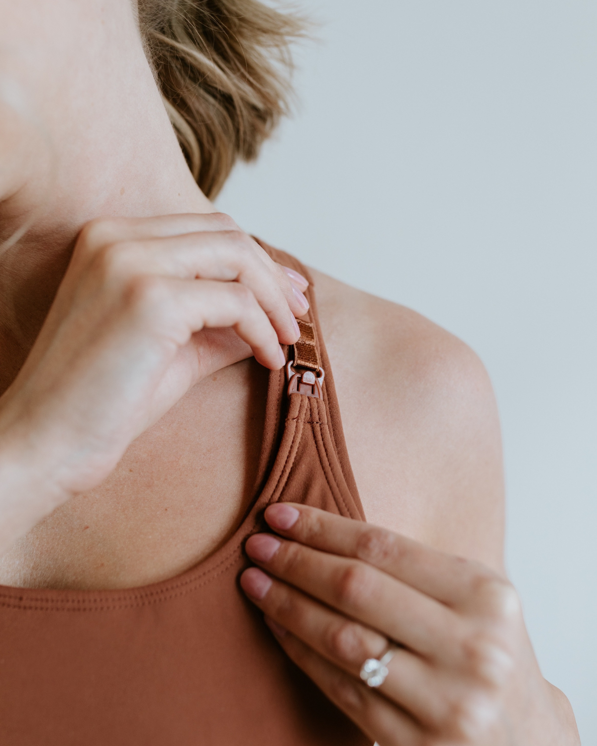 Close-up of a model unclipping the one-handed nursing clasp on a brown, maternity and nursing sports bra, highlighting functional nursing access. Premium maternity athletic and activewear by AXK.