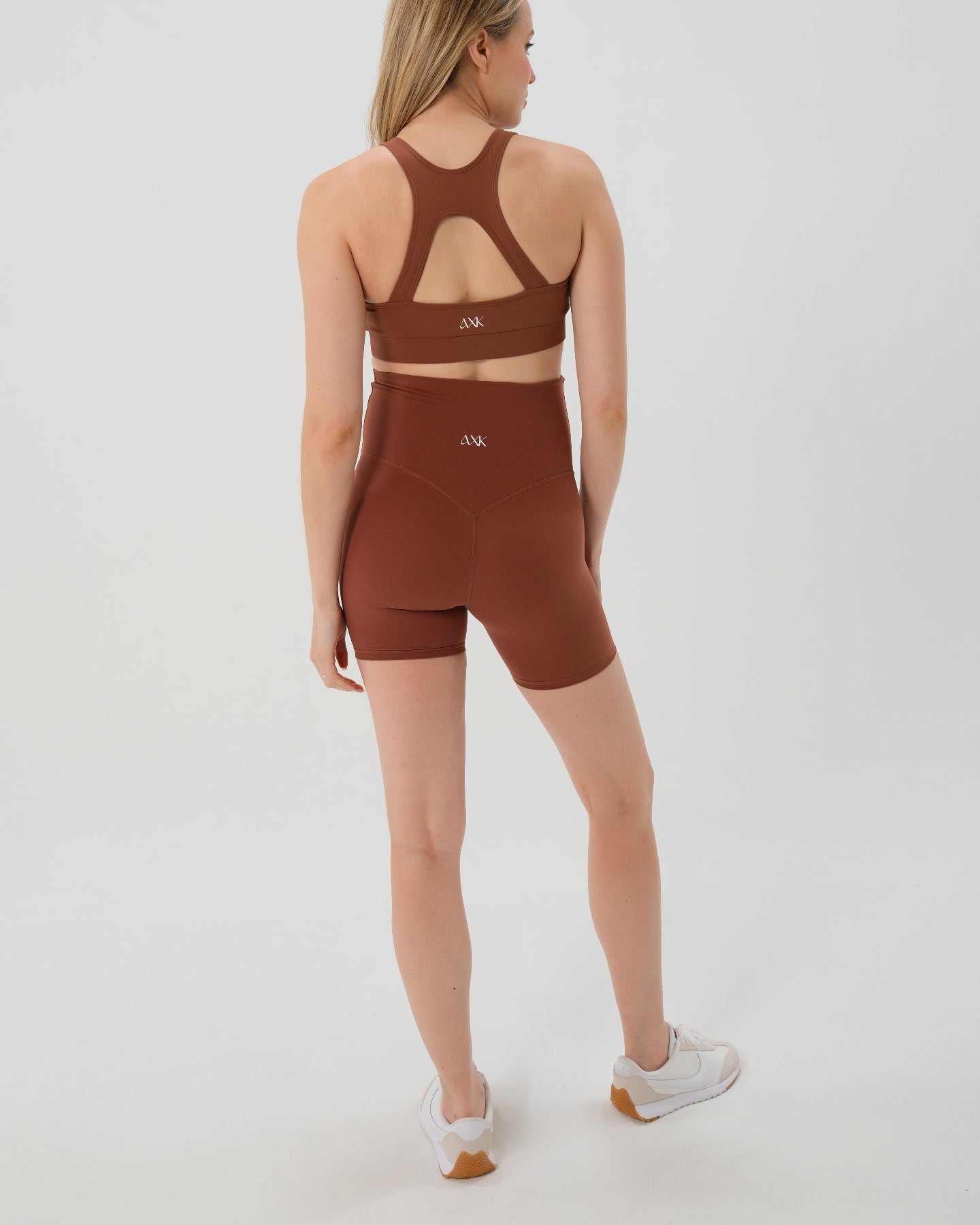 Pregnant woman wearing premium brown maternity bike shorts with a supportive high waist and matching high-impact, racerback maternity and nursing sports bra. Best reviewed 2026 premium maternity athletic and activewear by AXK, petite and tall friendly, in regular and plus size options. 