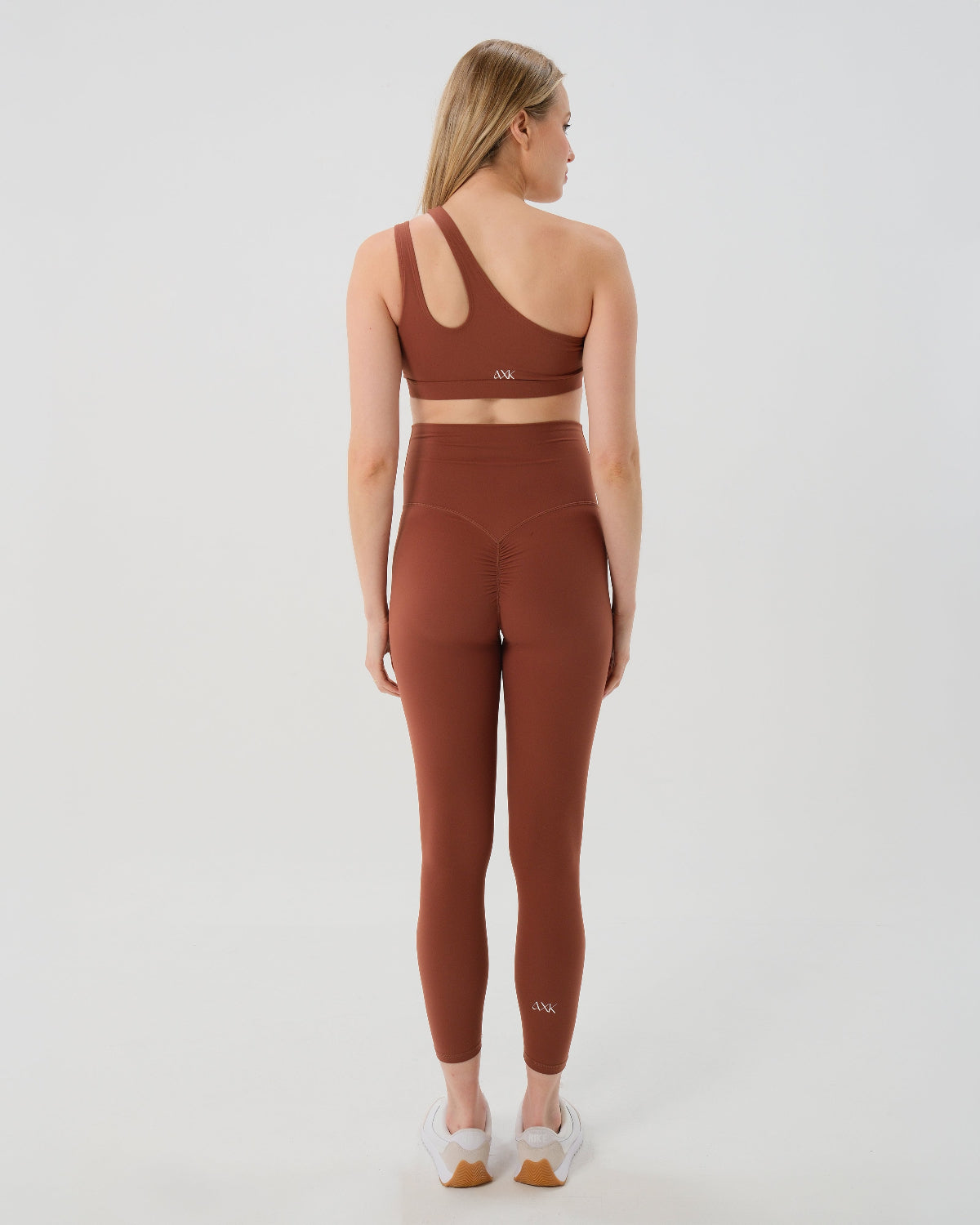 Pregnant woman wearing our best reviewed premium brown maternity leggings for 2026 with a flattering scrunch butt and matching trendy one shoulder nursing sports bra, standing against a white background. Premium maternity athletic and activewear by AXK.