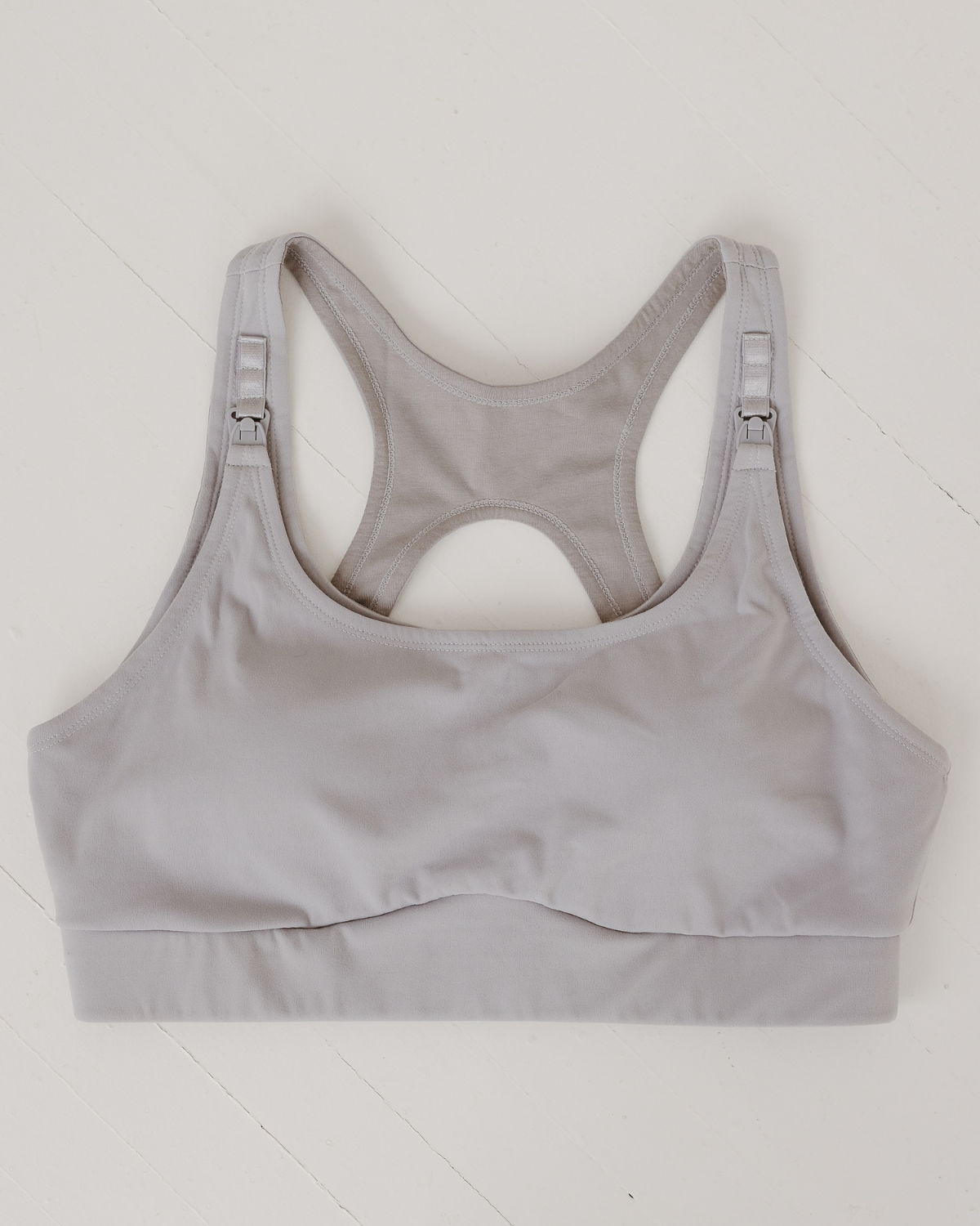 Flat lay of light-gray, high-impact, racerback nursing sports bra with clip-down straps and a smooth, seamless design, displayed on a white background. Premium maternity athletic and activewear by AXK.