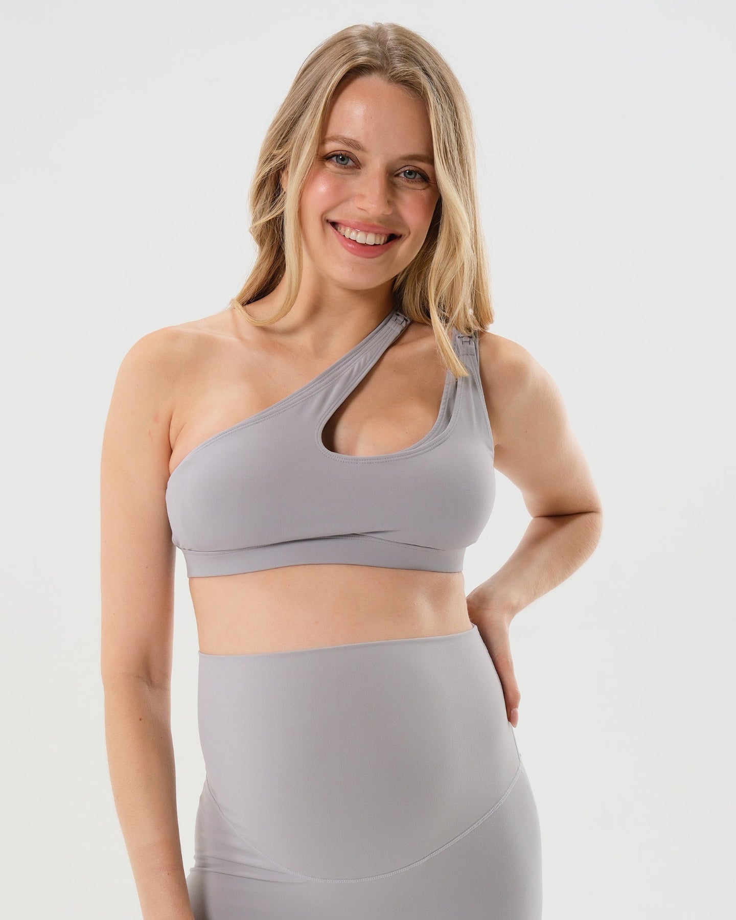 Light gray AXK one-shoulder maternity and nursing sports bra and matching leggings. The bra features one-handed clip access for easy breastfeeding. Our best reviewed 2026 premium maternity activewear by AXK is offered in petite and plus size.